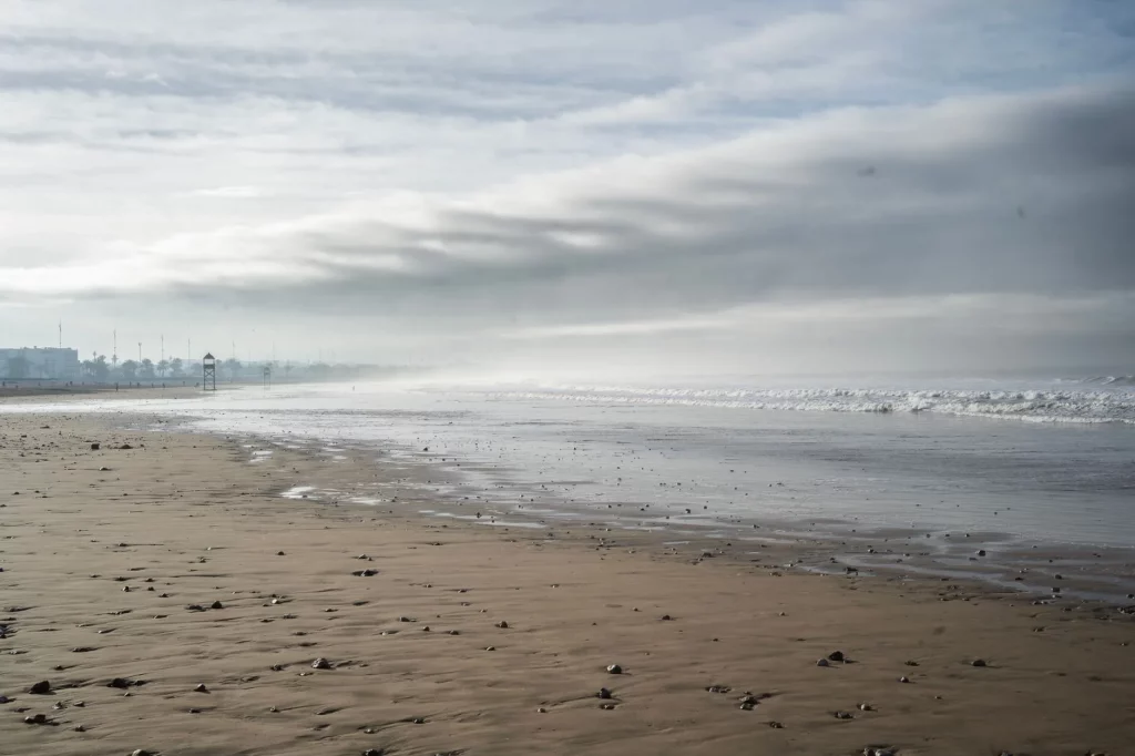 Wide sandy beach at low tide with breaking waves and a hazy coastline