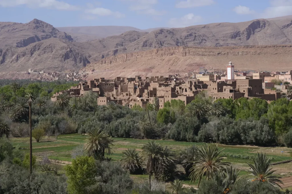 Earthen kasbah village among palm groves below dry mountains in Morocco