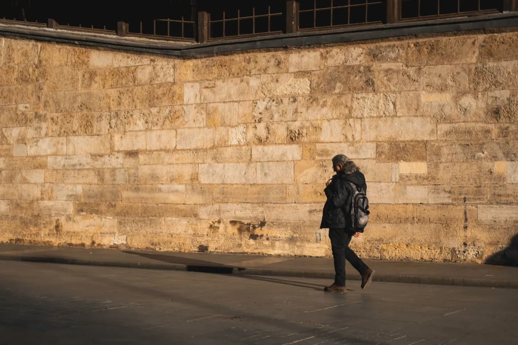 Traveller with a backpack walking alone along a sunlit stone wall