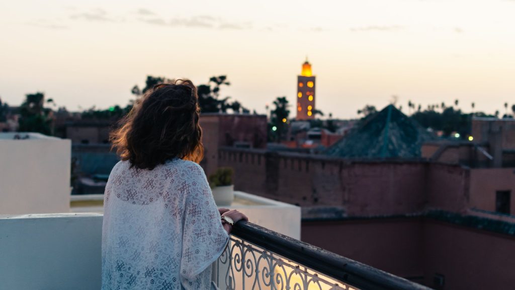 Traveller on a Marrakech hotel balcony at dusk, looking over the medina to the Koutoubia minaret