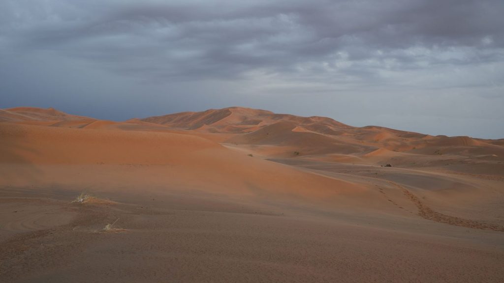 Vast, serene sand dunes of Erg Chebbi under a cloudy sky in Merzouga, Morocco.