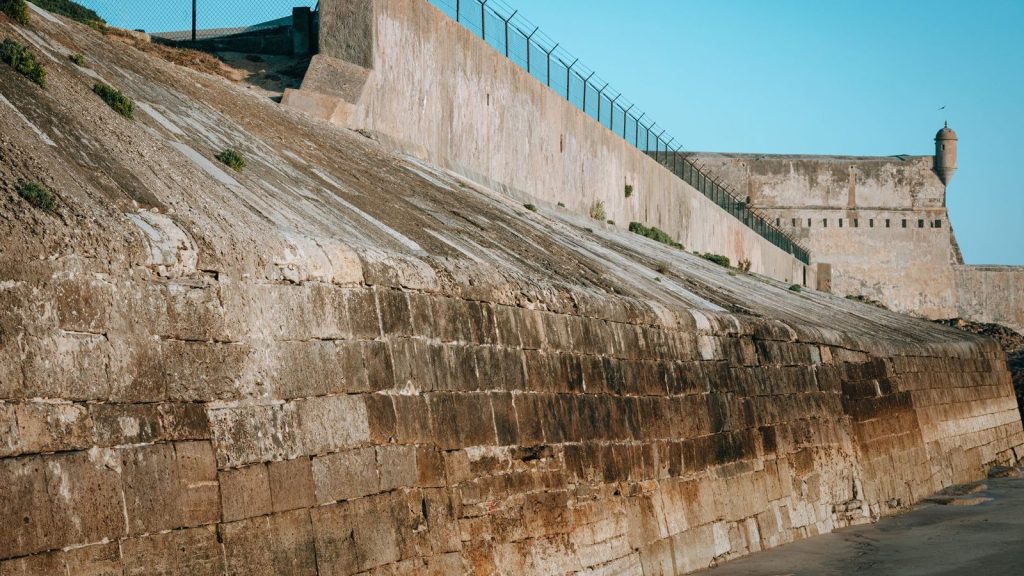 A rugged fortress wall with defensive features under a clear blue sky, showcasing historic architecture.