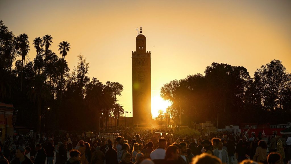 A bustling crowd gathers under the iconic Koutoubia Mosque tower at sunset in Marrakesh, Morocco.