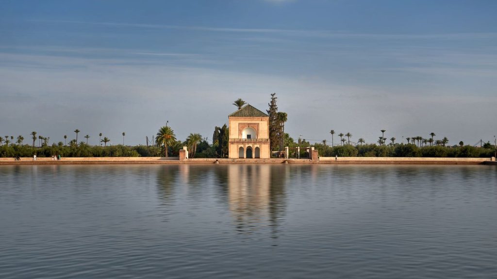 Tranquil view of Menara Gardens pavilion reflecting in water under a clear blue sky in Marrakech.