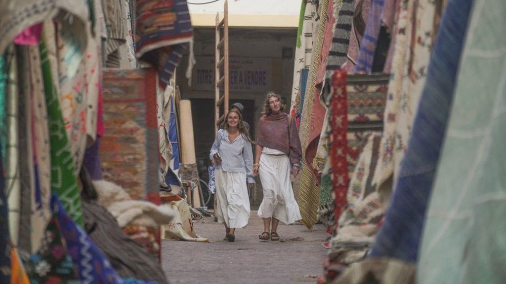 Two travellers walking together through a carpet market alleyway in Essaouira, Morocco