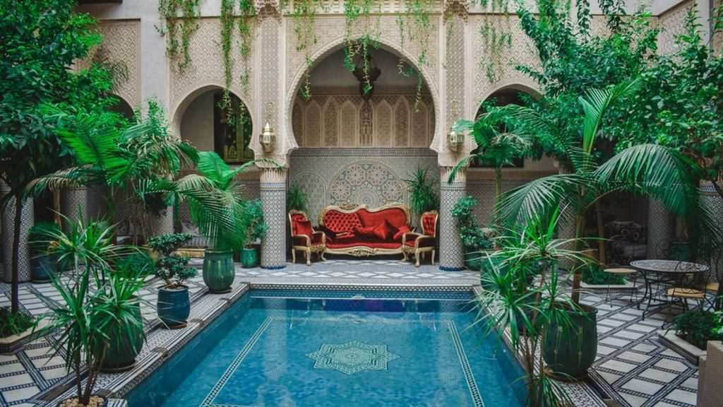 Courtyard of a traditional Moroccan riad with a tiled pool, arches and palms