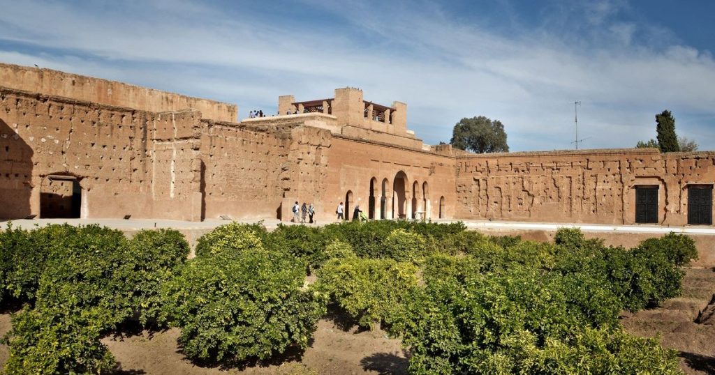 The red walls and orange trees of the El Badi Palace in Marrakech under a blue sky