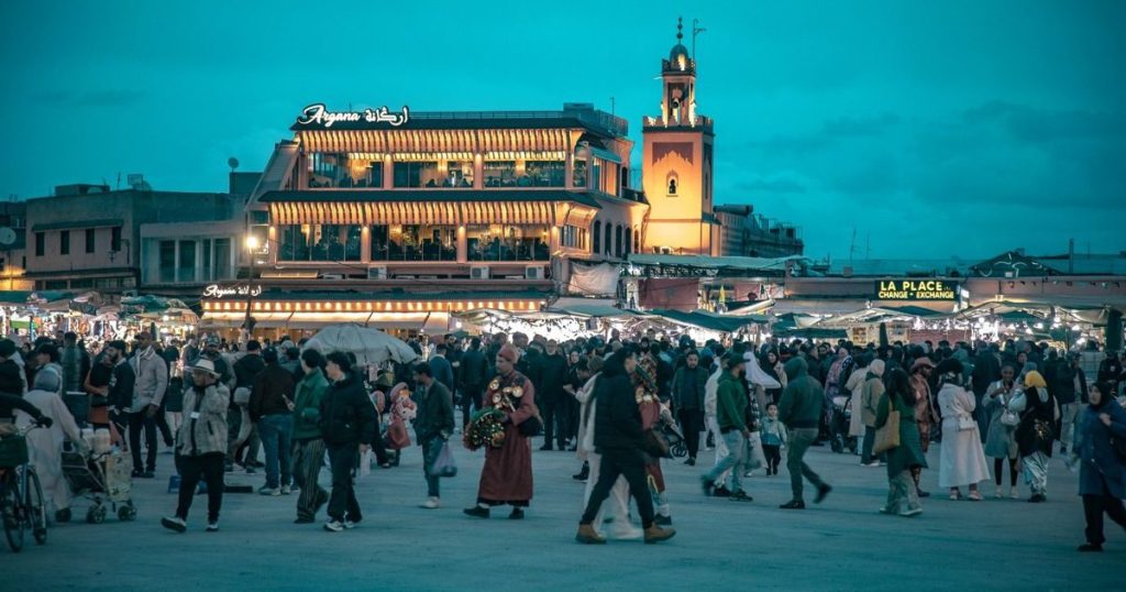 Jemaa el-Fna square in Marrakech at dusk, with the lit café terraces and the crowd
