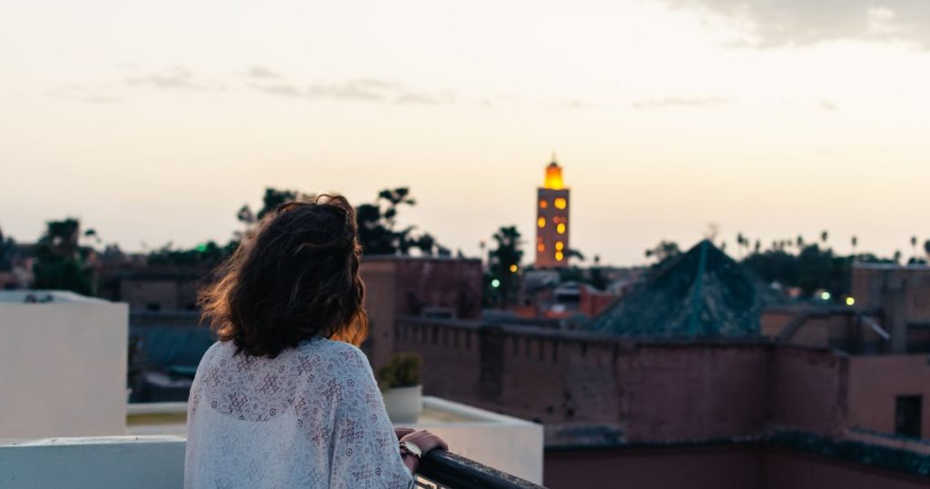 A woman on a roof terrace looking at the Koutoubia minaret lit at dusk in Marrakech