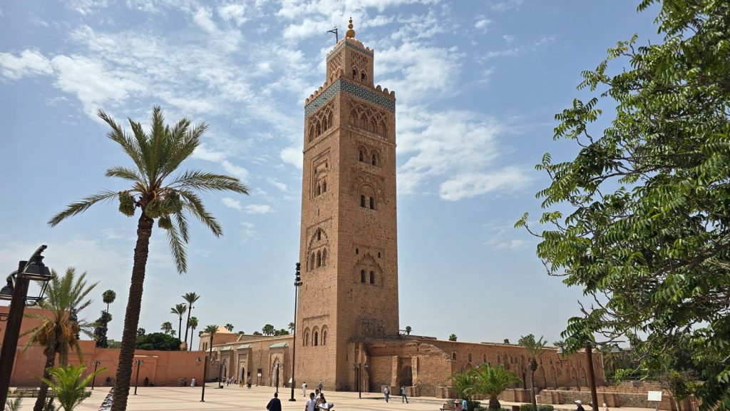 The Koutoubia mosque minaret in Marrakech under a blue sky, with palm trees on the square