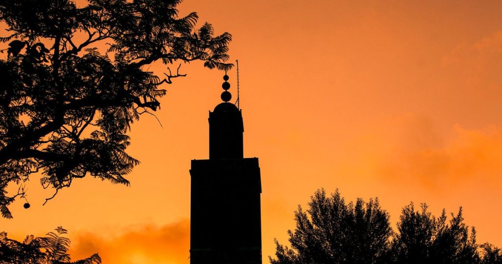 The silhouette of a minaret against an orange sunset sky in Morocco