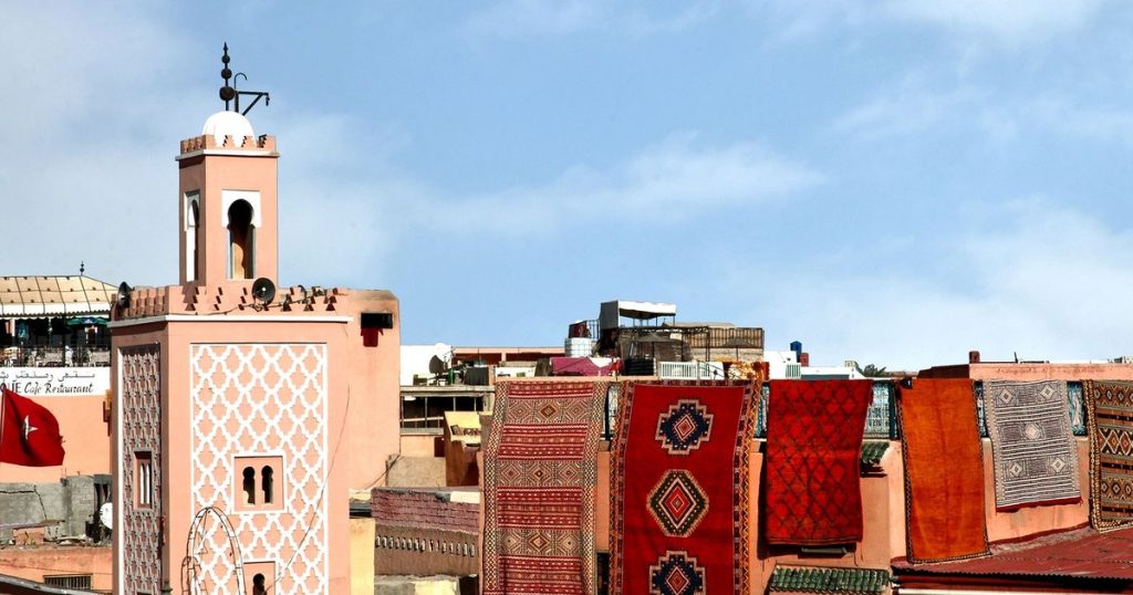 A minaret and Moroccan rugs hung over a rooftop in the Marrakech medina