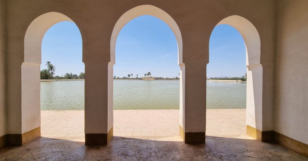 Three white arches framing a view over a large basin of water in Marrakech