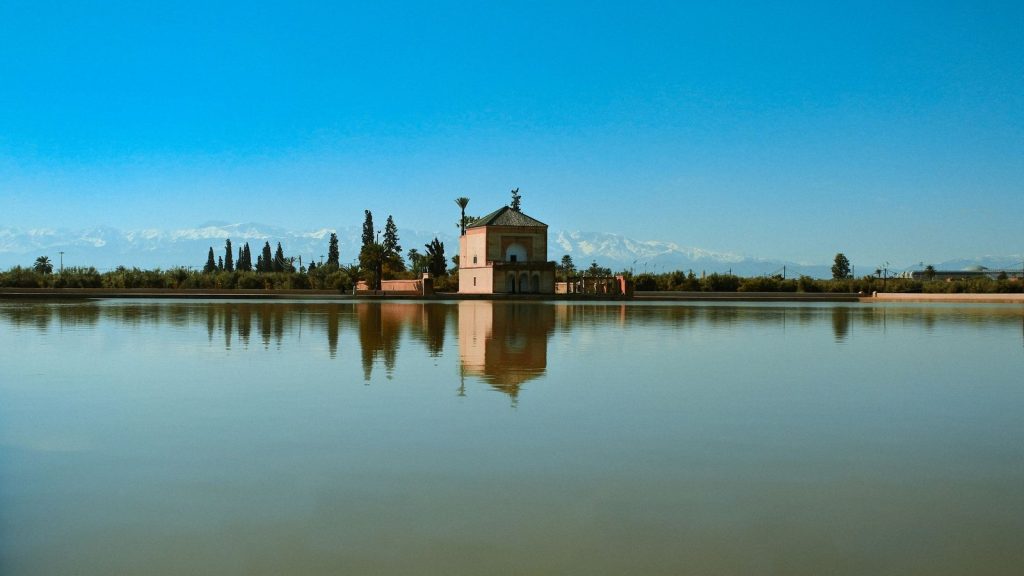 The Menara gardens pavilion in Marrakech reflected in its basin, with the snow-capped Atlas mountains behind